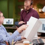 Mesa de trabalho de indústria com notebook exibindo campanha de marketing digital em Joinville e peça usinada ao lado