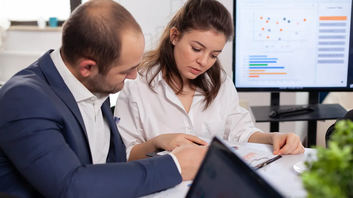 Duas pessoas discutindo as etapas de um funil de vendas B2B em uma parede de vidro com notas adesivas